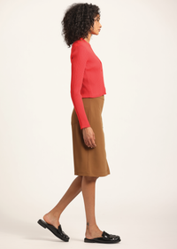 Woman wearing a red sweater and brown skirt on a white background