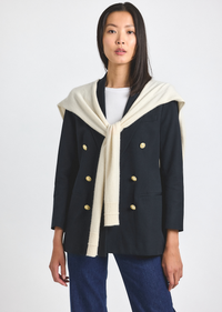 Woman wearing a navy coat with a cream sweater on a white background