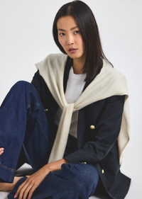 Woman wearing a navy coat with a cream scarf on a white background