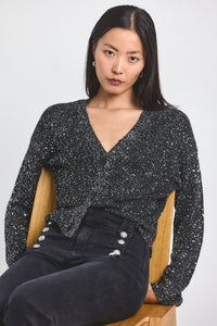 Woman wearing a black sequin top sitting on a wooden chair against a white background