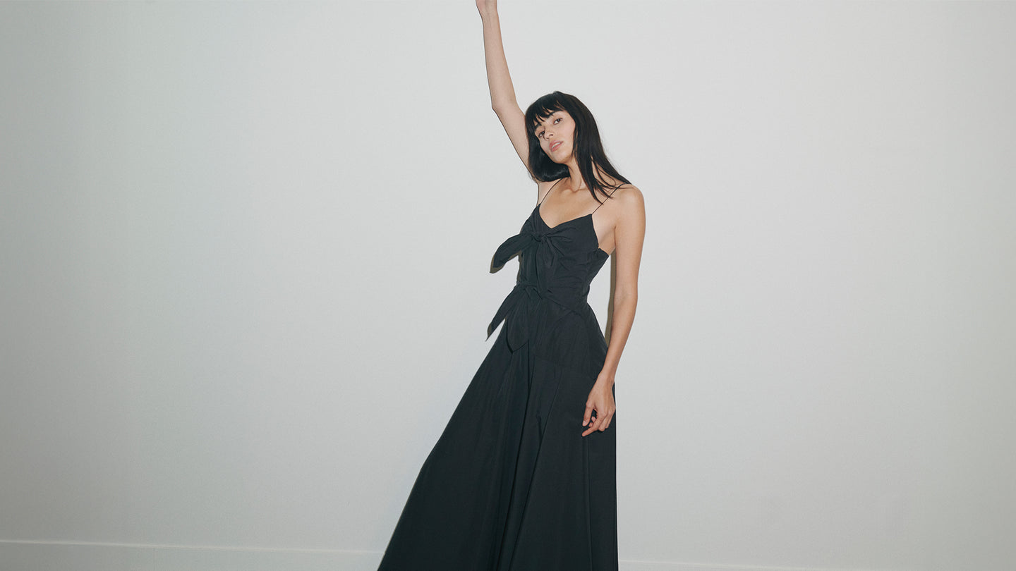 Woman in a black evening gown with a bow detail on a plain background