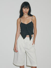 woman wearing white short bermudas and black top infront of white wall