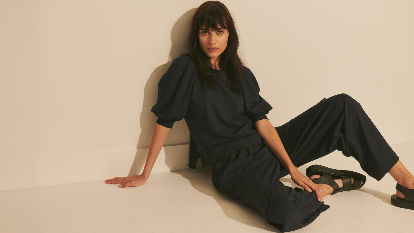 Woman in a black outfit sitting on a beige floor.