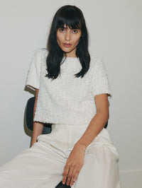 Woman wearing a textured white top and light-colored pants against a plain background