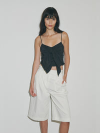 Woman wearing a black top and white pants against a plain background