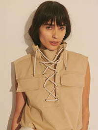 Woman wearing a beige sleeveless top with lace-up front against a plain background