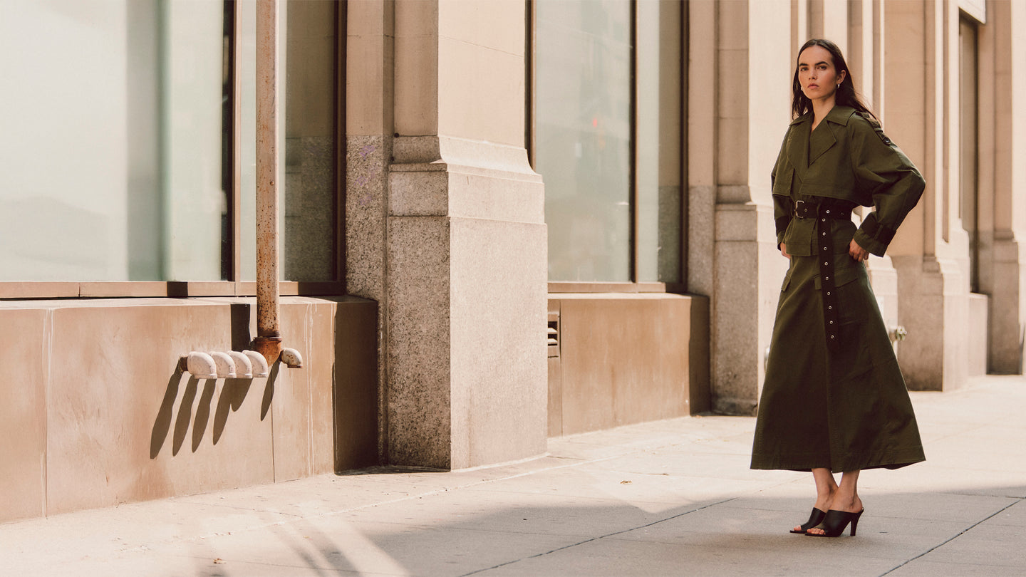 Woman wearing a long green coat standing in front of classical architecture.