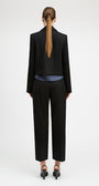 A model shown from the back wearing a black cropped blazer, black cropped trousers, a blue striped shirt, and black heels against a plain white studio background.