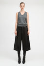 A model stands against a light gray studio background wearing a gray sleeveless knit top, wide-leg black cropped trousers, black leggings, and black pointed boots.