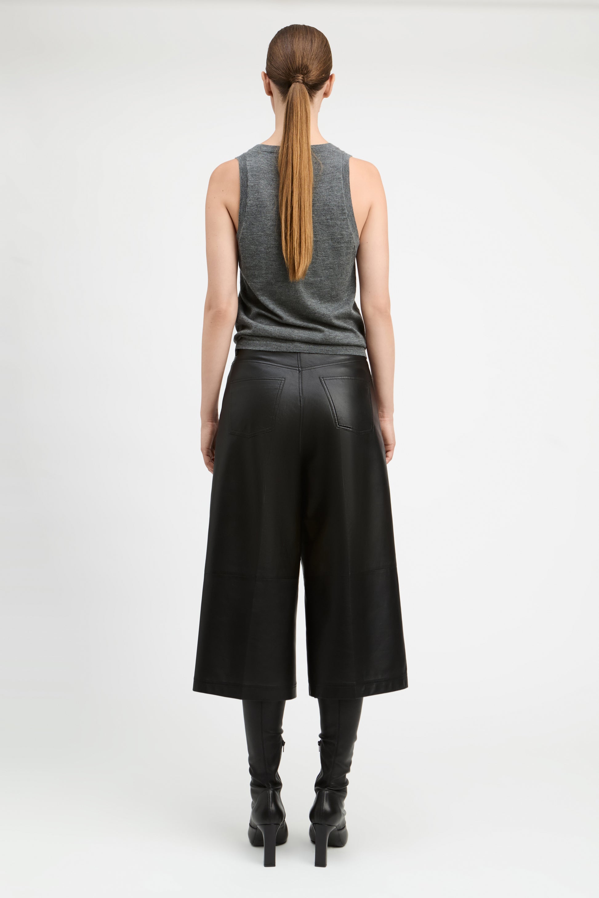 A model shown from the back wearing a gray sleeveless top, black wide-leg cropped pants, and black heeled boots against a plain light gray studio background.