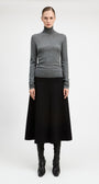 A model stands against a light gray studio background wearing a fitted gray turtleneck sweater, a long black skirt, and black knee-high boots.
