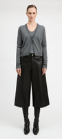 A model stands against a light gray studio background wearing a gray knit cardigan over a dark top, black wide-leg cropped trousers, black boots, and a black belt.