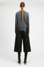 A model viewed from the back wearing a gray long-sleeve knit sweater, black wide-leg cropped pants, and black heeled boots against a plain light gray studio background.