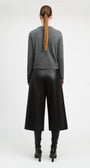 A model viewed from the back wearing a gray long-sleeve knit sweater, black wide-leg cropped pants, and black heeled boots against a plain light gray studio background.