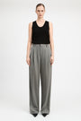 A model stands against a light gray studio background wearing a black sleeveless top and high-waisted, wide-leg gray trousers.