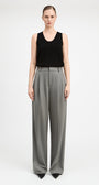 A model stands against a light gray studio background wearing a black sleeveless top and high-waisted, wide-leg gray trousers.