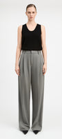 A model stands against a light gray studio background wearing a black sleeveless top and high-waisted, wide-leg gray trousers.