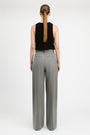 A woman shown from the back wearing a black sleeveless top and high-waisted, wide-leg gray trousers against a plain white studio background.