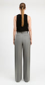 A woman shown from the back wearing a black sleeveless top and high-waisted, wide-leg gray trousers against a plain white studio background.