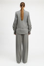 A model viewed from the back wearing a light gray two-piece suit with a structured blazer and wide-leg trousers, set against a plain white studio background.