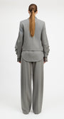 A model viewed from the back wearing a light gray two-piece suit with a structured blazer and wide-leg trousers, set against a plain white studio background.