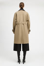 A model shown from the back wearing a mid-length beige trench coat with a black collar, black wide-leg cropped pants, and black heeled boots against a plain light gray studio background.