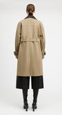 A model shown from the back wearing a mid-length beige trench coat with a black collar, black wide-leg cropped pants, and black heeled boots against a plain light gray studio background.