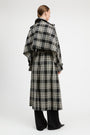 A model shown from the back wearing a long black and beige plaid coat with wide lapels and a self-tie belt, paired with black wide-leg trousers, against a plain light gray studio background.