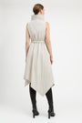 A model viewed from the back wearing a sleeveless, high-neck, belted midi dress in a light beige or off-white crinkled fabric, styled with black knee-high boots against a plain white studio background.