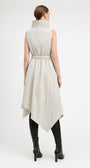 A model viewed from the back wearing a sleeveless, high-neck, belted midi dress in a light beige or off-white crinkled fabric, styled with black knee-high boots against a plain white studio background.