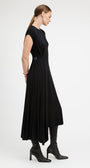 A woman modeling a black midi dress with a belted waist, shown from a side profile against a plain light gray studio background.