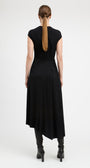 A woman viewed from the back wearing a black sleeveless midi dress with a gathered waist and black heeled ankle boots, against a plain light gray studio background.