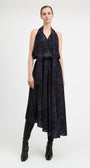 A model stands against a light gray studio background wearing a sleeveless dark navy midi dress with a blue abstract pattern, black knee-high boots, and black leggings.