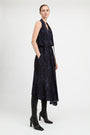 A model wearing a sleeveless dark navy midi dress with a subtle tonal floral pattern, styled with black knee-high leather boots against a light gray studio background.