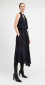 A model wearing a sleeveless dark navy midi dress with a subtle tonal floral pattern, styled with black knee-high leather boots against a light gray studio background.