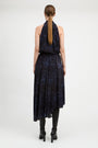 A woman viewed from the back wearing a sleeveless dark navy dress with a blue abstract print and black knee-high boots against a light gray studio background.