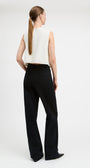 A woman shown from the back wearing a sleeveless white top and black wide-leg trousers against a plain light gray studio background.