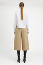 A woman shown from the back wearing a white long-sleeve blouse, beige wide-leg cropped pants, and black heeled boots against a plain light gray studio background.