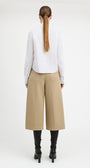 A woman shown from the back wearing a white long-sleeve blouse, beige wide-leg cropped pants, and black heeled boots against a plain light gray studio background.