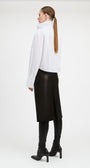 A woman shown from the back wearing a white high-neck long-sleeve top, a black midi skirt, black leggings, and black heeled ankle boots, photographed against a plain light gray studio background.