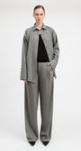 A model stands against a light gray studio background wearing a matching gray two-piece set consisting of a long-sleeve button-front overshirt and wide-leg trousers, styled over a black top and black pointed shoes.