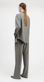 A model shown from the back wearing a matching gray two-piece lounge set consisting of a long-sleeve button-up shirt and wide-leg trousers, photographed against a seamless white studio background.
