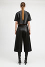 A model shown from the back wearing a black cropped short-sleeve top and matching black wide-leg cropped pants, paired with black knee-high boots against a plain light gray studio background.