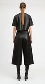 A model shown from the back wearing a black cropped short-sleeve top and matching black wide-leg cropped pants, paired with black knee-high boots against a plain light gray studio background.