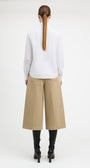 A model shown from the back wearing a white long-sleeve blouse, beige wide-leg cropped trousers, and black heeled boots against a plain white studio background.