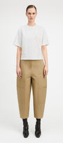 A model stands against a light gray studio background wearing a white short-sleeve top with textured embroidery, beige wide-leg cropped pants with side pockets, and black ankle boots.