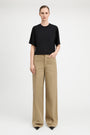 A model stands against a light gray studio background wearing a black short-sleeve crewneck top and beige wide-leg trousers.