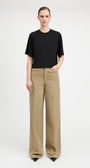 A model stands against a light gray studio background wearing a black short-sleeve crewneck top and beige wide-leg trousers.