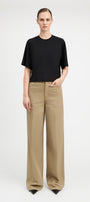 A model stands against a light gray studio background wearing a black short-sleeve crewneck top and beige wide-leg trousers.