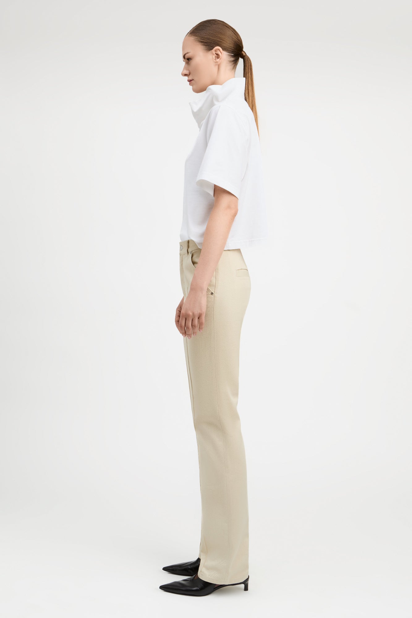 Woman wearing straight cut parchment color jeans with white top, side view. 